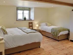 A bedroom with two beds, a window with a vase, wooden flooring, and a chair.