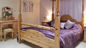 Ein Himmelbett mit Holzgestell und violetter Bettwäsche.