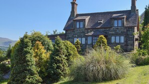 A stone house with two chimneys, surrounded by lush greenery and hills in the background. - 2 bedroom accommodation in Llandygai, near Bangor (Llandygai, near Bangor)