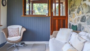 A cozy room with a wicker chair, a white sofa, and a stone wall. - 2 bedroom accommodation in Llandygai, near Bangor (Llandygai, near Bangor)
