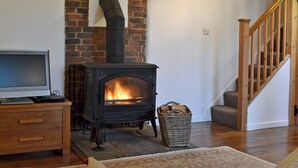 Una sala de estar acogedora con una chimenea de ladrillo, un televisor sobre un mueble de madera y una escalera a la derecha.