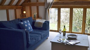 Una sala de estar acogedora con un sofá azul, una mesita de centro blanca y vistas a la naturaleza a través de amplias ventanas.