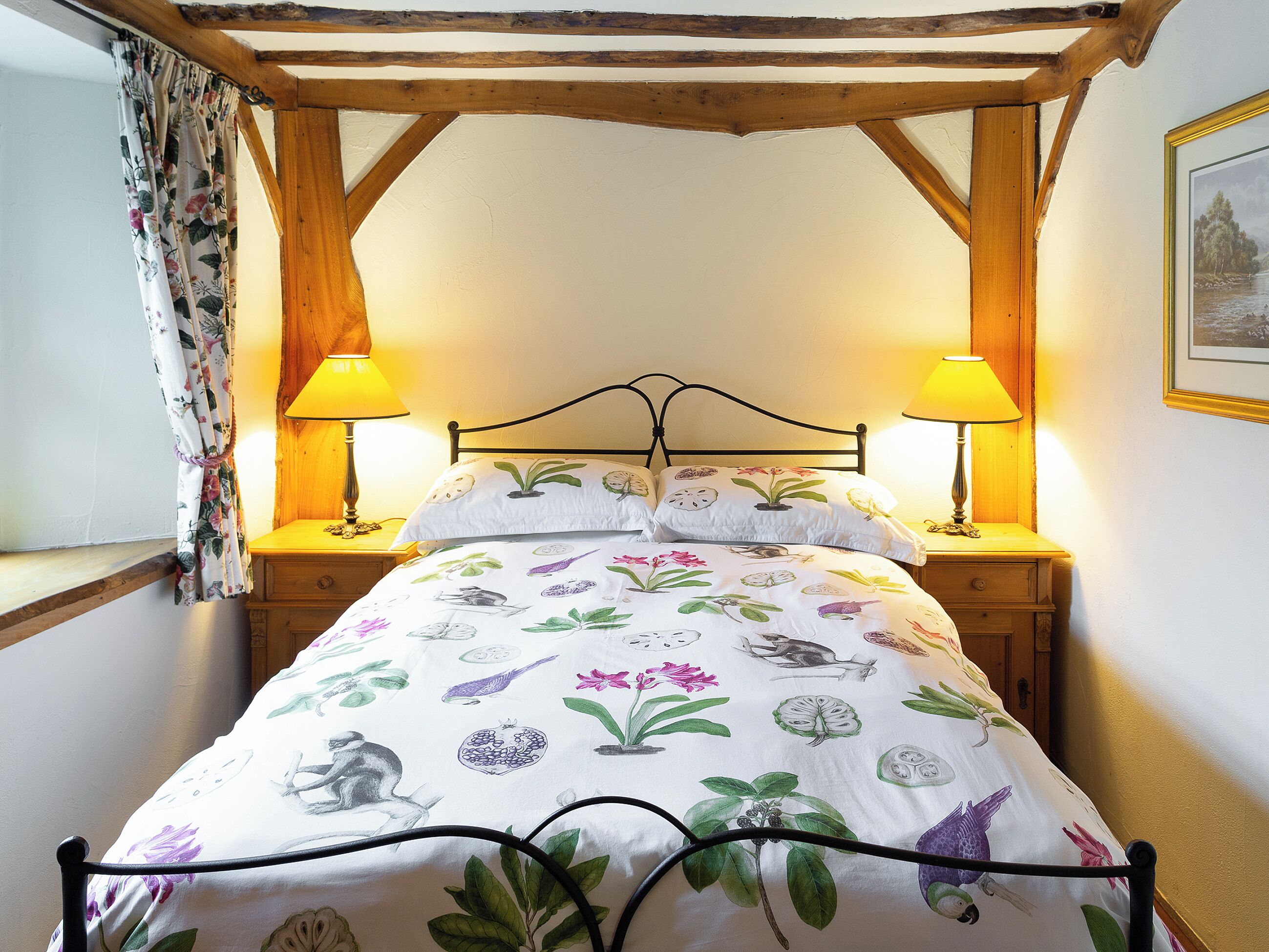 A bedroom with a wooden ceiling, two bedside lamps, a floral bedspread, and a framed picture on the wall.