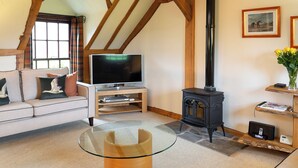 A living room with a glass-top coffee table, a sofa with cushions, a television, a black wood-burning stove, and a window with curtains. - 2 bedroom accommodation in Kinross, near Perth (Kinross, near Perth)