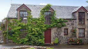 A stone house with a red door, ivy-covered walls, and flower planters. - 2 bedroom accommodation in Kinross, near Perth (Kinross, near Perth)