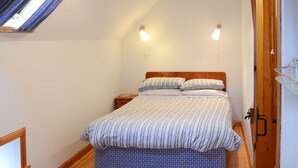A bedroom with a bed, bedside tables, a wooden floor, a skylight, and a bathroom with a sink. - 2 bedroom accommodation in John O&rsquo; Groats (John O&rsquo; Groats)