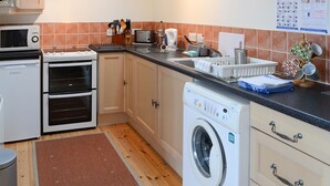A compact kitchen with a microwave, toaster, oven, and washing machine. - 2 bedroom accommodation in John O&rsquo; Groats (John O&rsquo; Groats)
