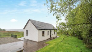 A white building with a sloped roof, a paved driveway, and a grassy area with trees. - 2 bedroom accommodation in Achnamara, near Lochgilphead (Achnamara, near Lochgilphead)