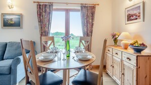 A dining area with a table set for four, chairs, a sofa, a cabinet, and a window with curtains. - 2 bedroom accommodation in Achnamara, near Lochgilphead (Achnamara, near Lochgilphead)