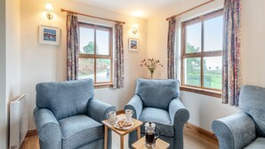 A room with two blue armchairs, a small wooden table with a coffee pot and cups, and a radiator. - 2 bedroom accommodation in Achnamara, near Lochgilphead (Achnamara, near Lochgilphead)