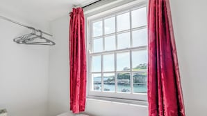 A bedroom with a bed, a window with curtains, and a view of the sea.