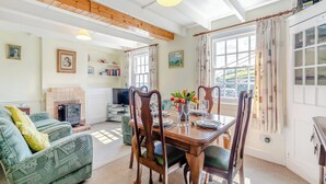 A cozy living room with a fireplace, a dining table set for four, and a large window with curtains.