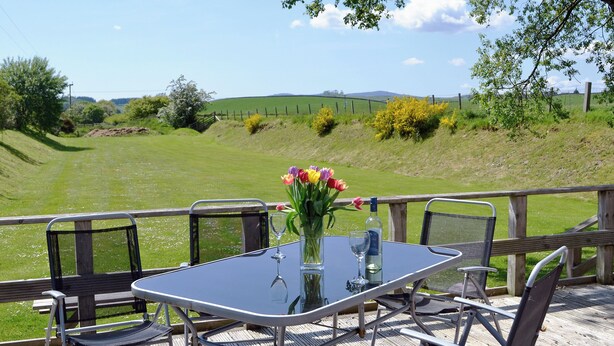 A table with chairs and a vase of flowers, overlooking a grassy field with a wooden fence. - 3 bedroom accommodation in Bridge of Dee, near Castle Douglas (Bridge of Dee, near Castle Douglas)