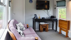 A room with a purple sofa, a small wooden table, a desk with a computer, a television, and a window with a view. - 3 bedroom accommodation in Bridge of Dee, near Castle Douglas (Bridge of Dee, near Castle Douglas)