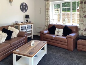 A living room with two brown leather sofas, a wooden coffee table, a wall clock, and a window with curtains.