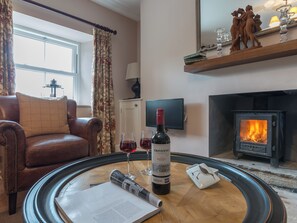 Una sala de estar con un sofá de cuero, una chimenea, un televisor y una botella de vino sobre una mesa auxiliar.