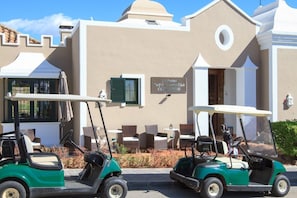 A golf cart parked in front of a building with a sign reading 'La Resina Golf & Country Club CLUBHOUSE'.