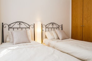 A bedroom with two beds, a bedside lamp, and a wooden wardrobe.