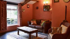 Un salon chaleureux avec un plafond en bois, un canapé en cuir marron, un fauteuil en osier, une table basse en bois et un tapis à motifs.
