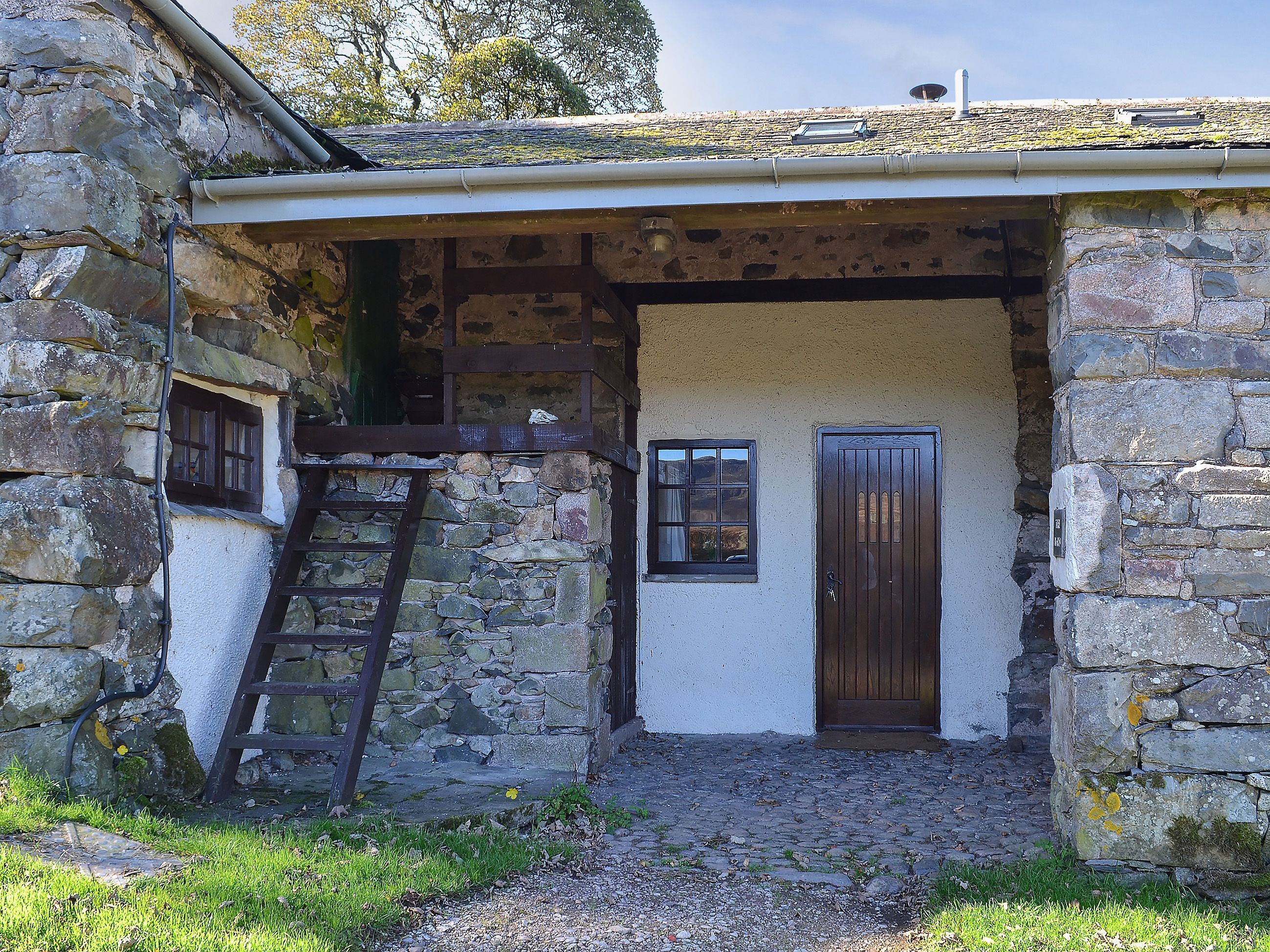 Un edificio de piedra con puerta de madera, una ventana y una escalera que lleva a un nivel superior.