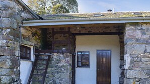 Un bâtiment en pierre avec une porte en bois, une fenêtre et une échelle menant à un niveau supérieur.
