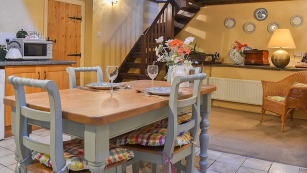 Un coin repas avec une table en bois dressée pour deux personnes, un four à micro-ondes et un escalier menant à l’étage supérieur.