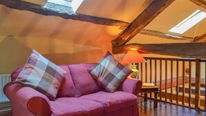 Une pièce chaleureuse avec un canapé rouge, deux coussins à motifs, un plafond en bois et une lampe.