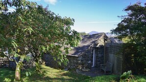 Un bâtiment en pierre doté d’un toit en pente, entouré d’une clôture en bois et d’un arbre.