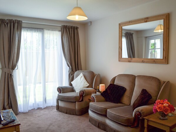 A living room with two armchairs, a small table with a vase of flowers, a lamp, and a mirror on the wall.
