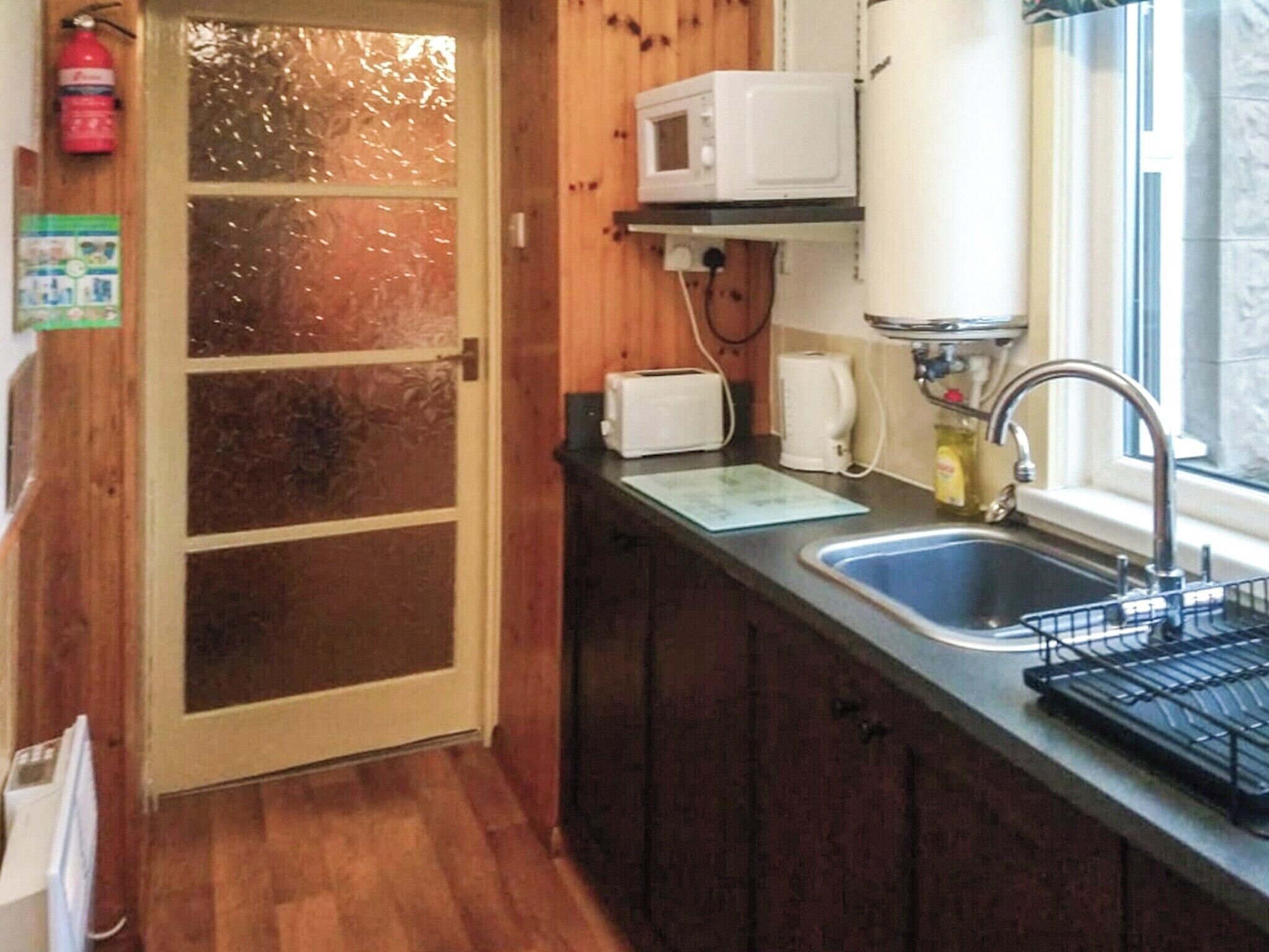 A kitchen with a wooden door, a microwave on a shelf, a toaster, and a sink with a faucet.