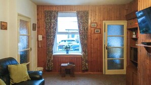 A room with a wooden paneled wall, a black leather sofa, a small wooden table, and a door with frosted glass panels. - An affordable terraced cottage just 50 yards from the harbour at Seahouses. (Seahouses, near Bamburgh)