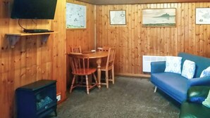 A room with wooden walls, a blue sofa, a wooden dining table with chairs, a small heater, and a TV mounted on the wall. - An affordable terraced cottage just 50 yards from the harbour at Seahouses. (Seahouses, near Bamburgh)