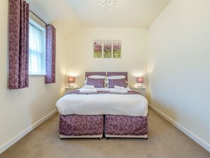A bedroom with a bed, two bedside tables, a window with curtains, and wall art. - 2 bedroom accommodation in Wimborne (Wimborne)