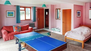 Een kamer met een tafeltennistafel, een rode bank, een bed en een klein tafeltje met een stoel.