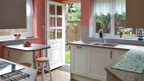 Une cuisine de taille réduite avec des meubles blancs, un plan de travail en bois, un évier et une fenêtre donnant sur un jardin.