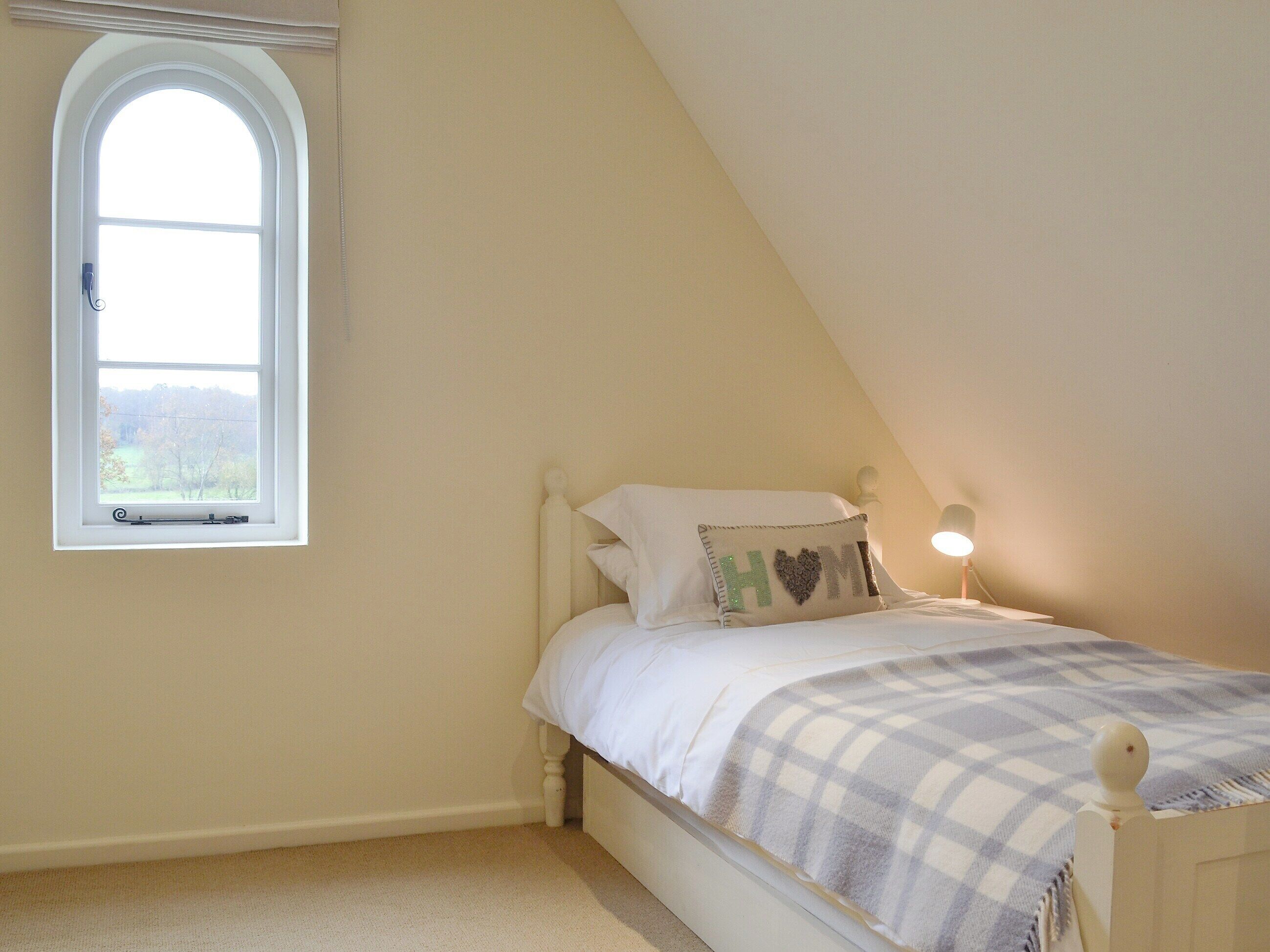 A single bed with a checkered blanket, a pillow with a heart design, and a small bedside table with a lamp.