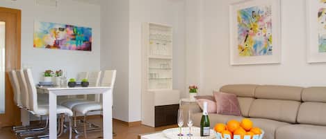 A modern living room with a dining area, white furniture, and artwork on the walls.