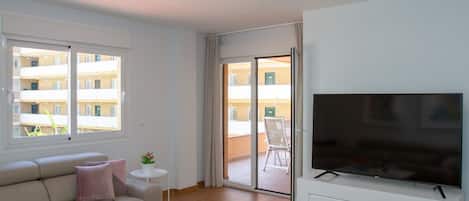 Una sala de estar moderna con un sofá, un televisor y un balcón con vistas a edificios.