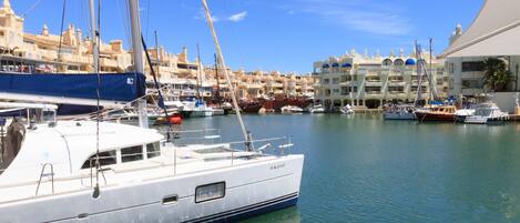 A marina with boats docked, a clear blue sky, and buildings in the background.