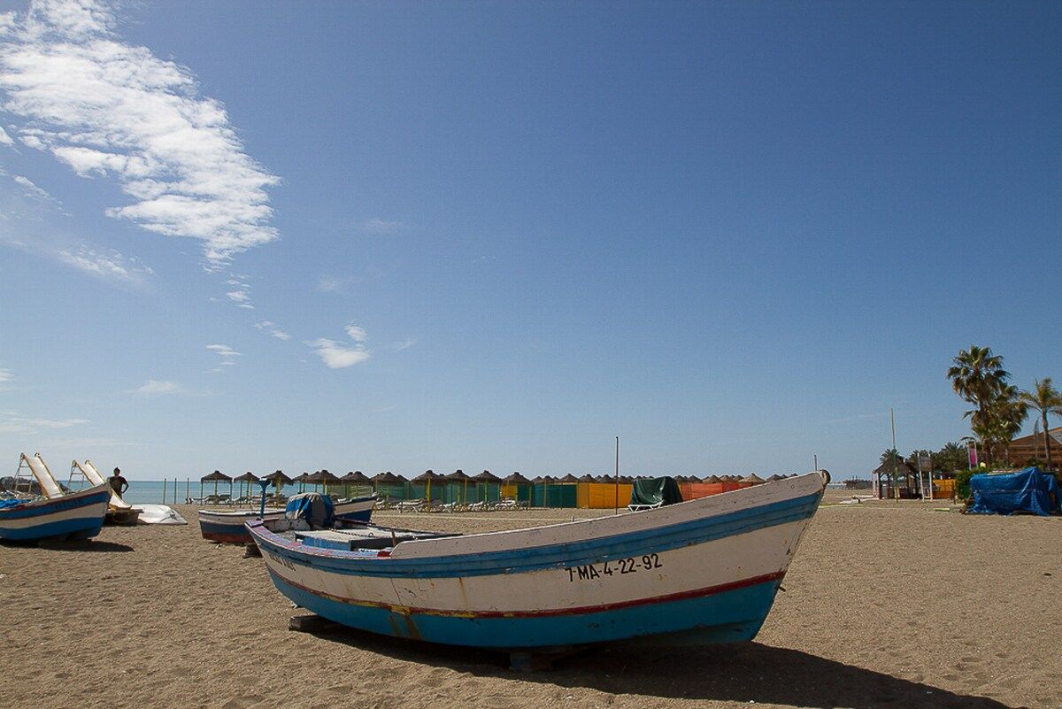 A beach with several boats and beach huts in the background.