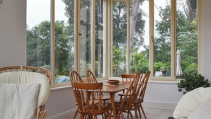 Zona pranzo con un tavolo grande e sedie, un lampadario e ampie finestre con vista sugli alberi.