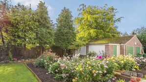 Ein Garten mit verschiedenen Blumen und ein kleines Backsteinhaus mit grünen Türen.