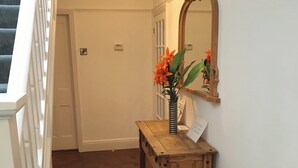 Un banco de madera con un florero, un espejo y una puerta en un pasillo.
