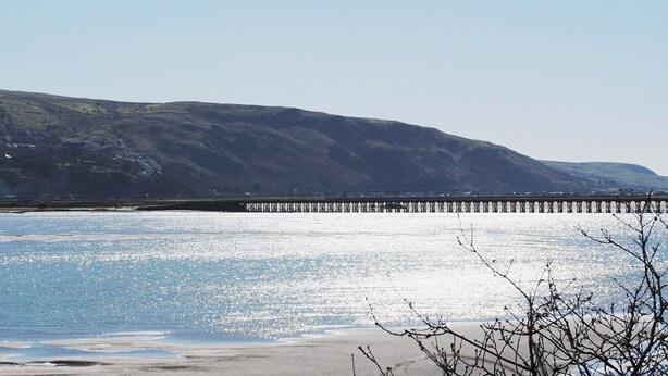 Un paisaje costero con un muelle que se adentra en el agua, rodeado de colinas.