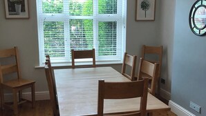 Un comedor con mesa y sillas de madera, una ventana con persianas y cuadros en las paredes.