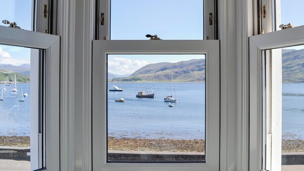 Blick durch ein Fenster auf Boote auf einem See, umgeben von Hügeln.