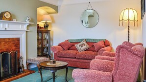 Ein gemütliches Wohnzimmer mit Kamin, einem roten Sofa, einem passenden Sessel, einem runden Spiegel und einer Lampe.