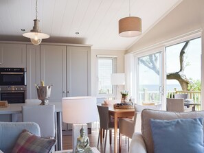 A modern kitchen with built-in appliances, a dining area with a table and chairs, and large windows offering a view of the outdoors.