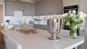 A kitchen with grey cabinets, a wooden cutting board, a metal container with a bottle, and a vase with flowers on the counter. - 2 bedroom accommodation in Corton, near Lowestoft (Corton, near Lowestoft)