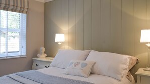 A bedroom with a bed, two bedside lamps, a nightstand with a sculpture, and a window with blinds. - 2 bedroom accommodation in Corton, near Lowestoft (Corton, near Lowestoft)